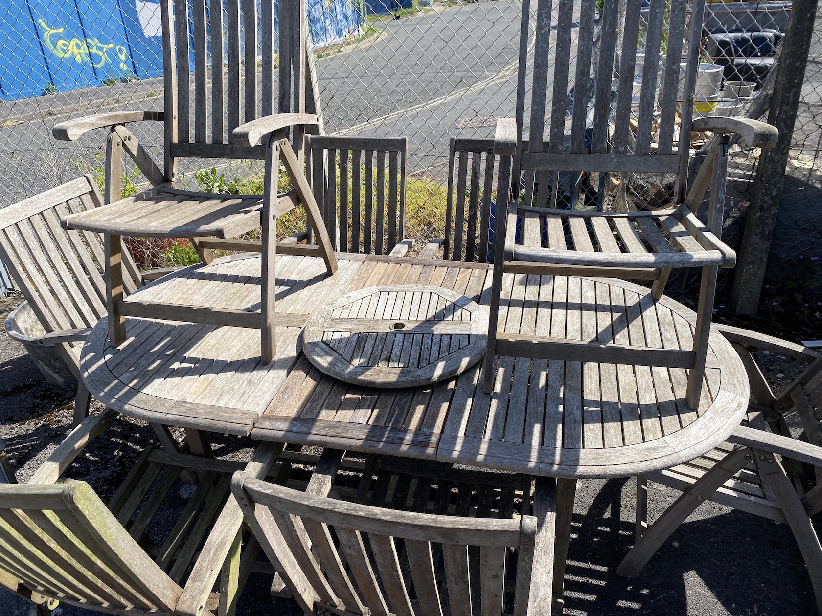 A weathered teak oval extending dining table and eight folding elbow chairs (7 plus 1), table 208cm extended, depth 110cm, height 76cm